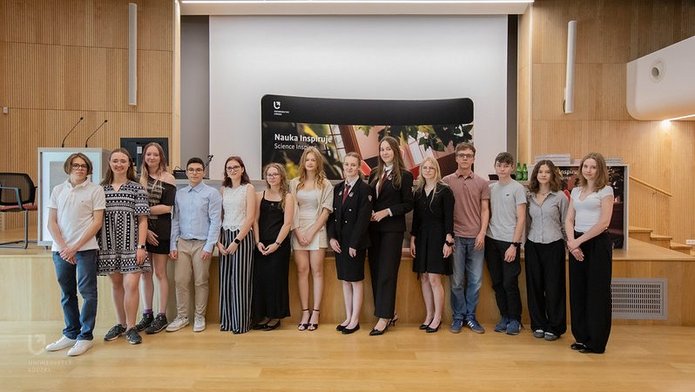 Grupa młodych osób - laureatów konkursu Laboratorium Innowacji - stoją w auli, pozując do zdjęcia