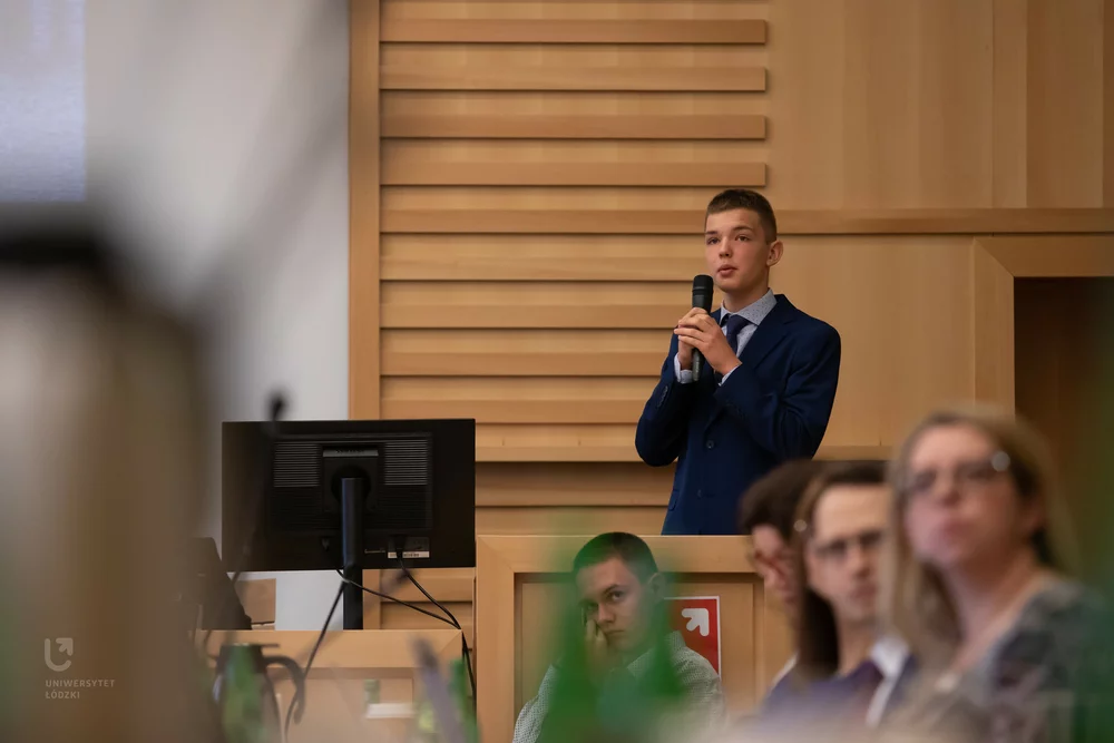 A student standing in the assembly hall with a microphone – a participant of the “Talented Secondary School Student - Brilliant University Student” programme